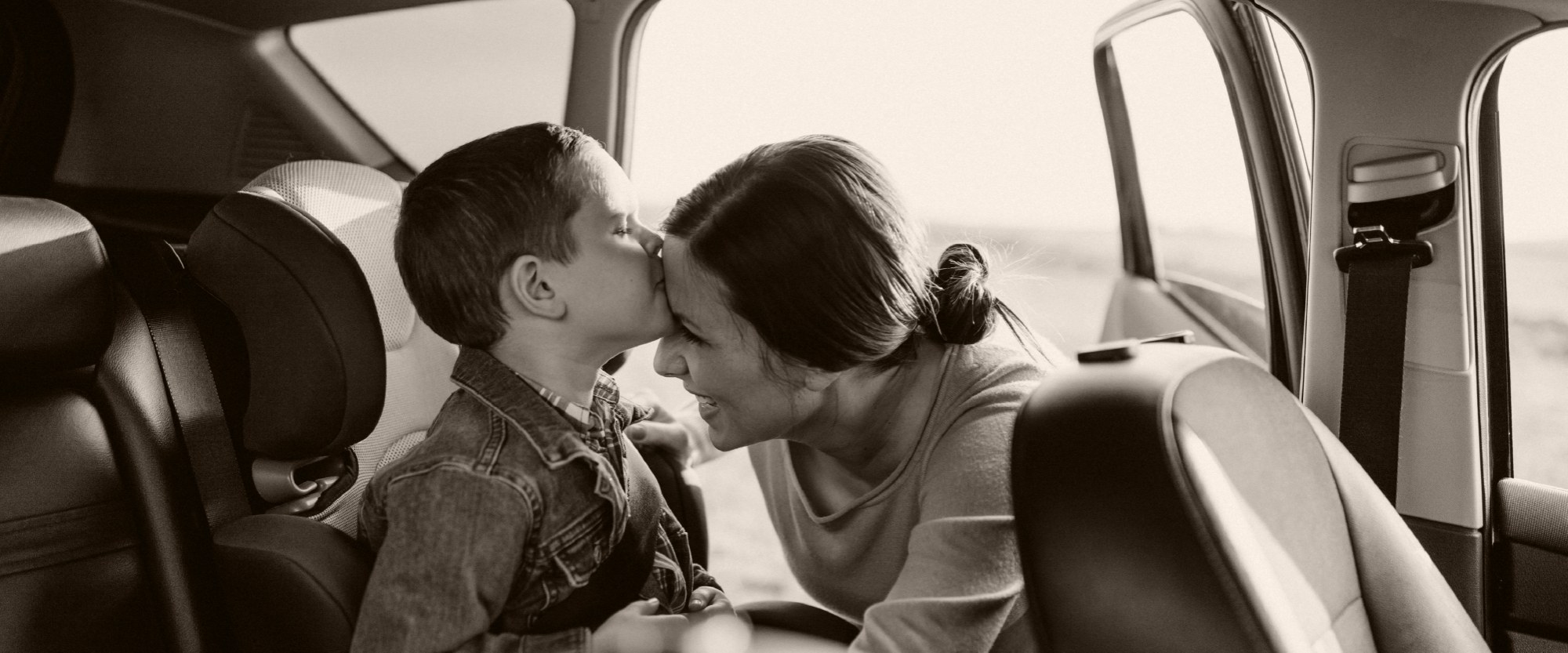 Photo of kid kissing mom after being buckled into car seat in back