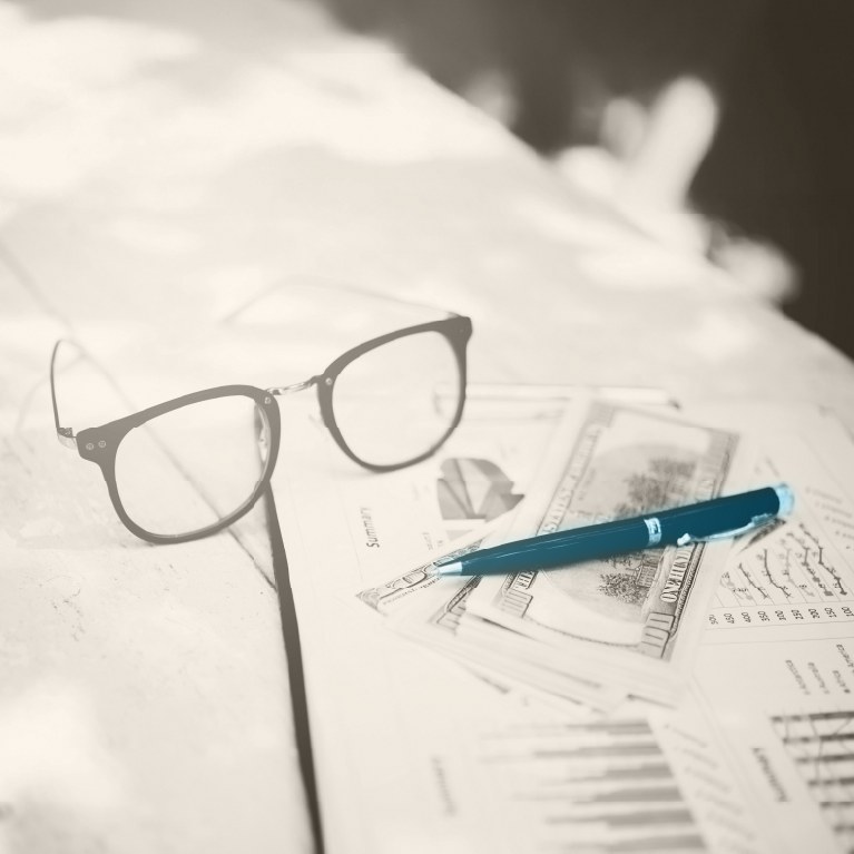 a desk with bills, a pen  and glasses