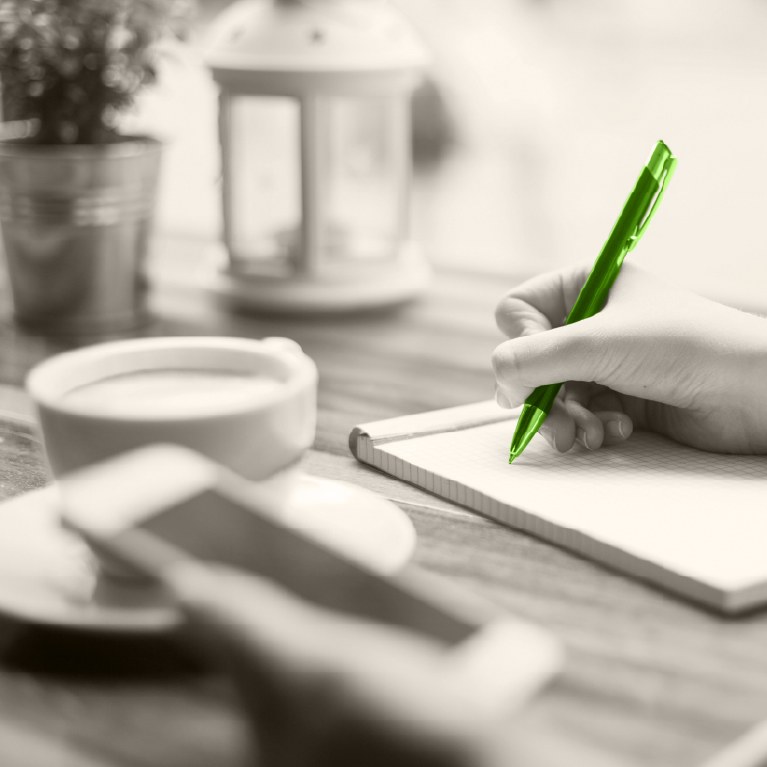hand writing in notebook with a green pen