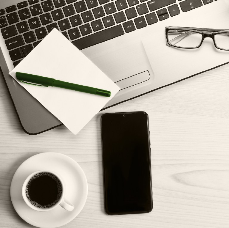 desk with laptop and phone with a cup of coffee next to them