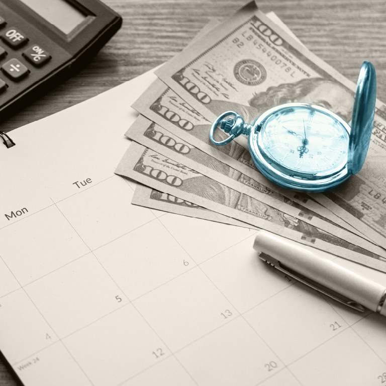blue watch over some money and a calendar on a desk with a calculator
