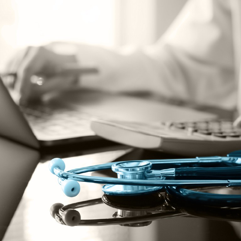 blue stethoscope next to someone working on a laptop with calculator next to it