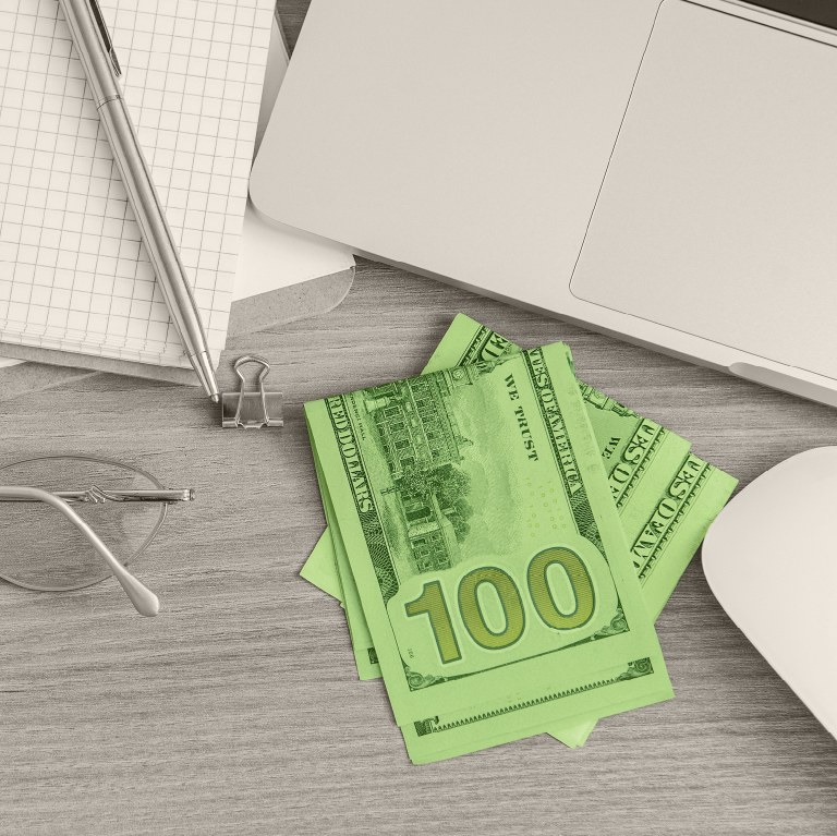 green cash on a table next to a notebook pen and computer