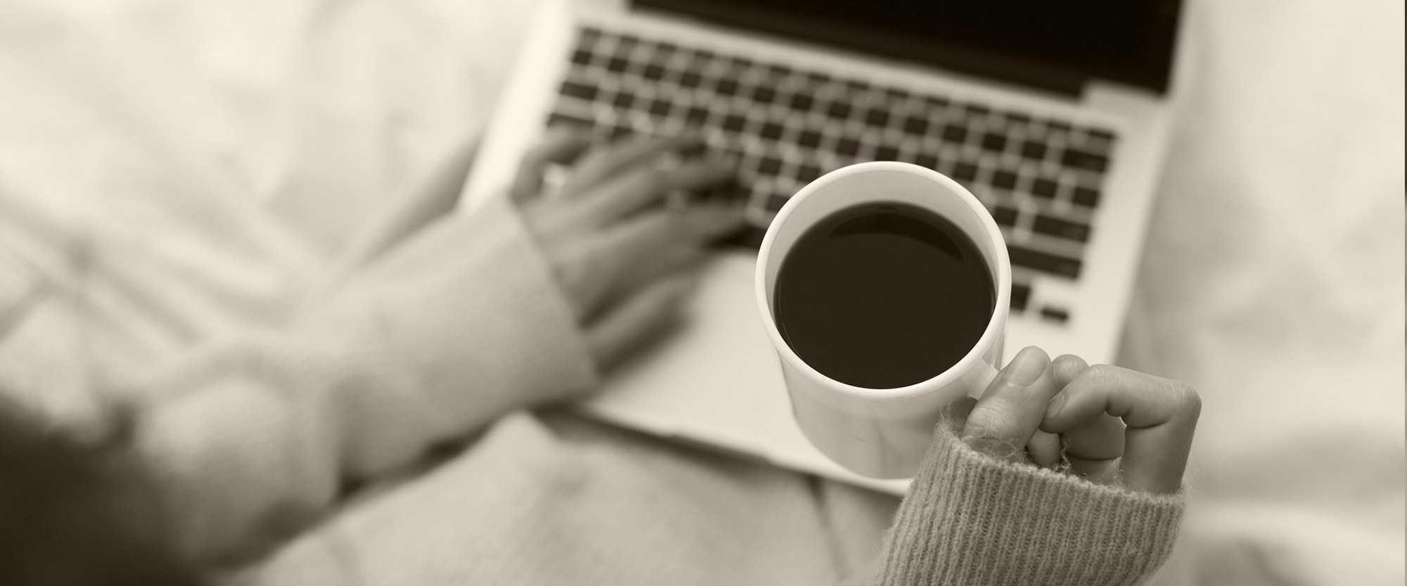 hand holding coffee cup over laptop on person's lap