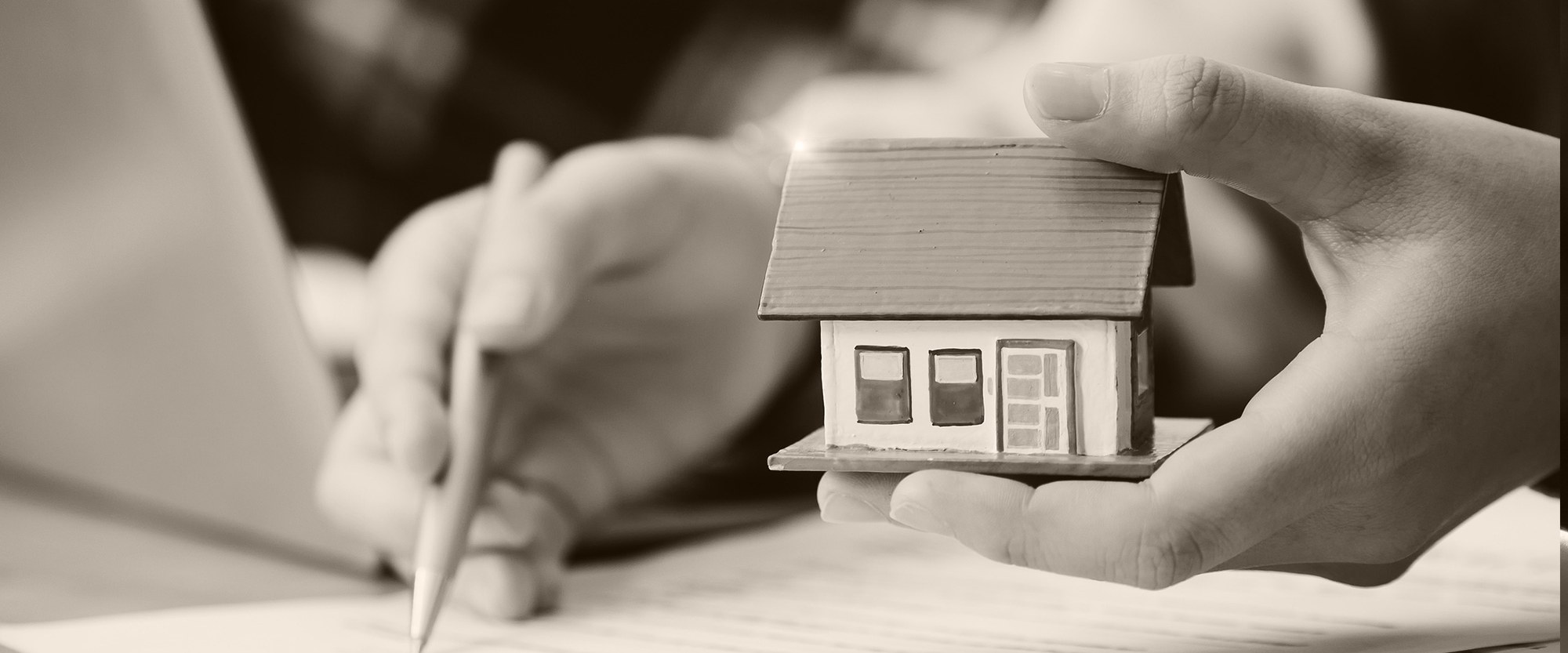 hand holding a mini home while other hand filling out paperwork