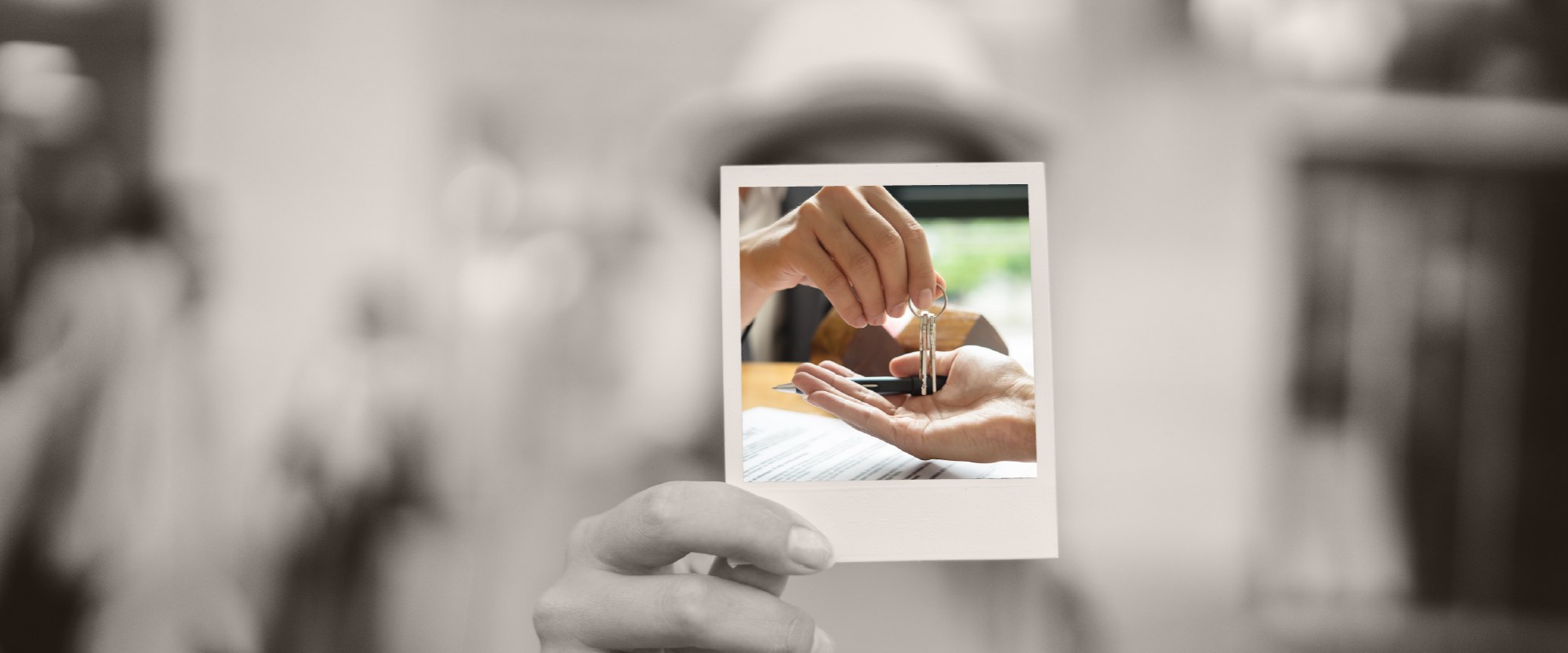 hand holding a key above someone's hand after signing home loan paperwork on a desk