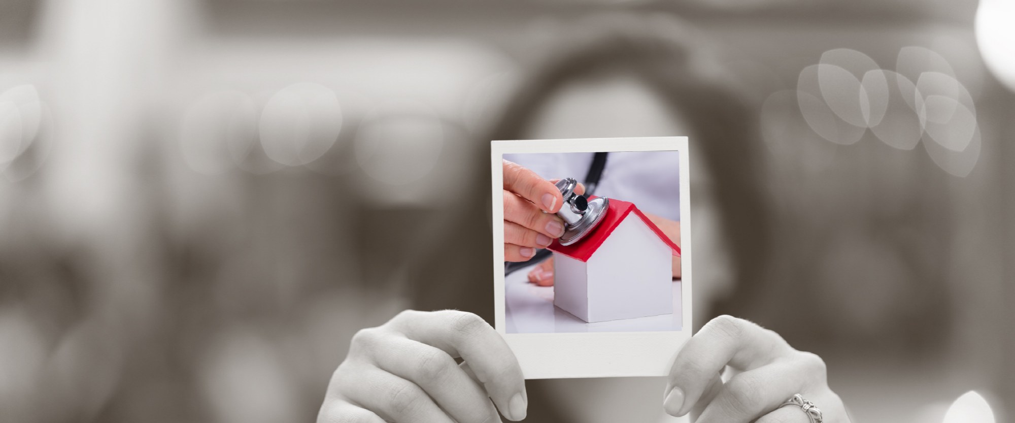 hand holding a polaroid of mini wooden house with stethoscope to the roof