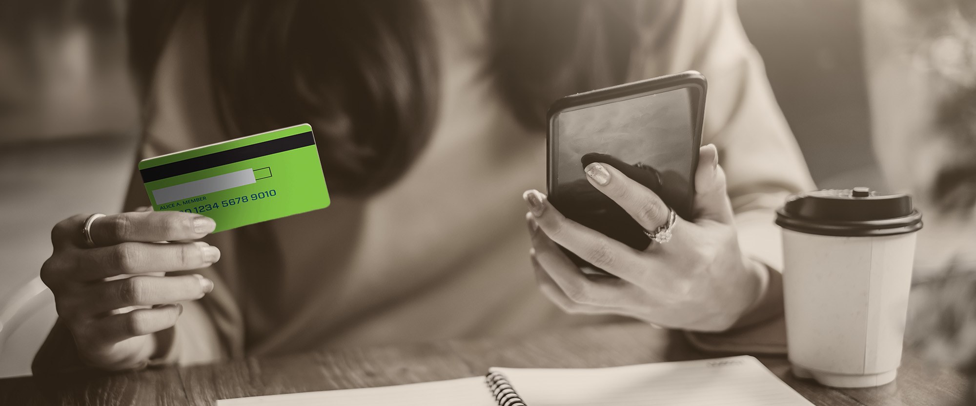 Woman at desk holding credit card and looking at phone