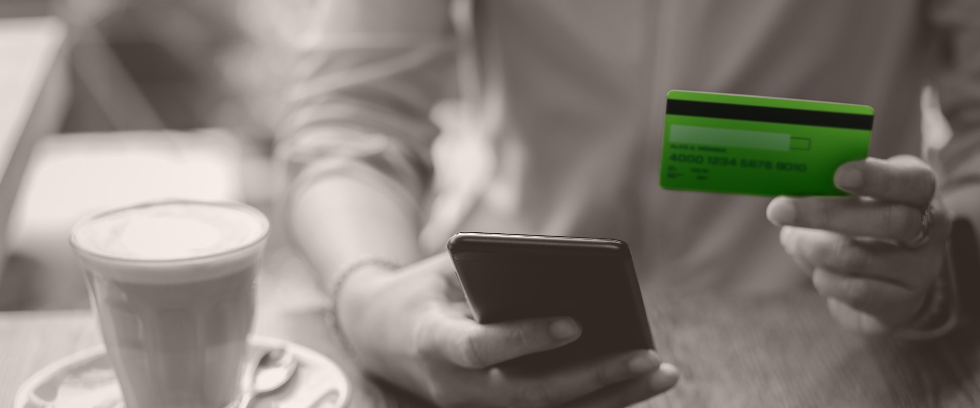 man with coffee cup holding green platinum card while on his smartphone