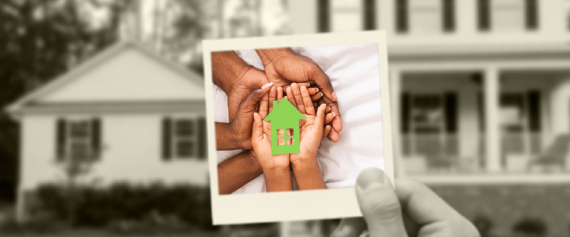 family set of hands holding a green cutout house in a polaroid being held in front of a house