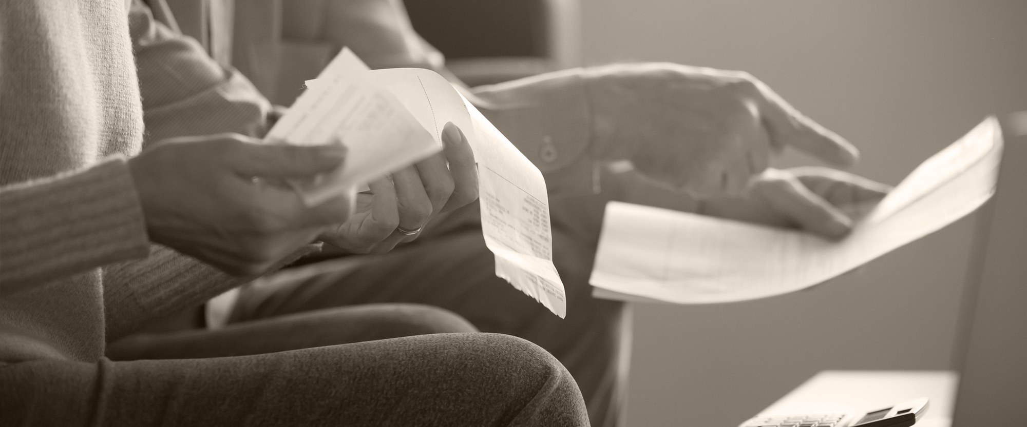 couple sitting on sofa  as hands holding bills in front of a laptop