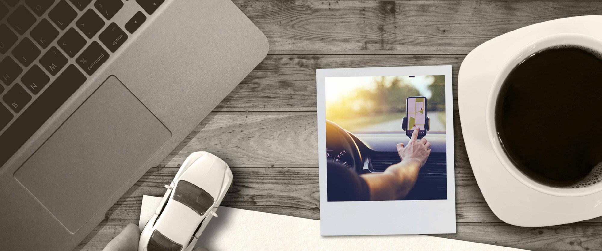 smartphone with an image of an auto on the road next to a laptop and coffee cup