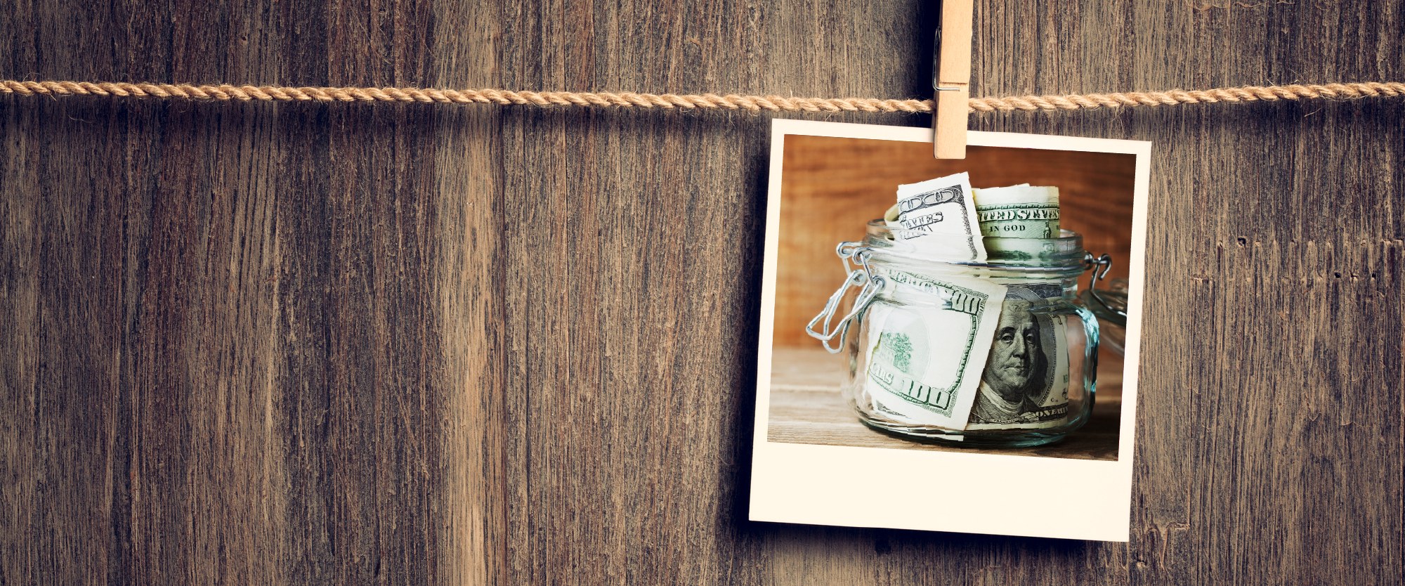 wood board background with a polaroid of a jar stuffed with hundred dollar bills