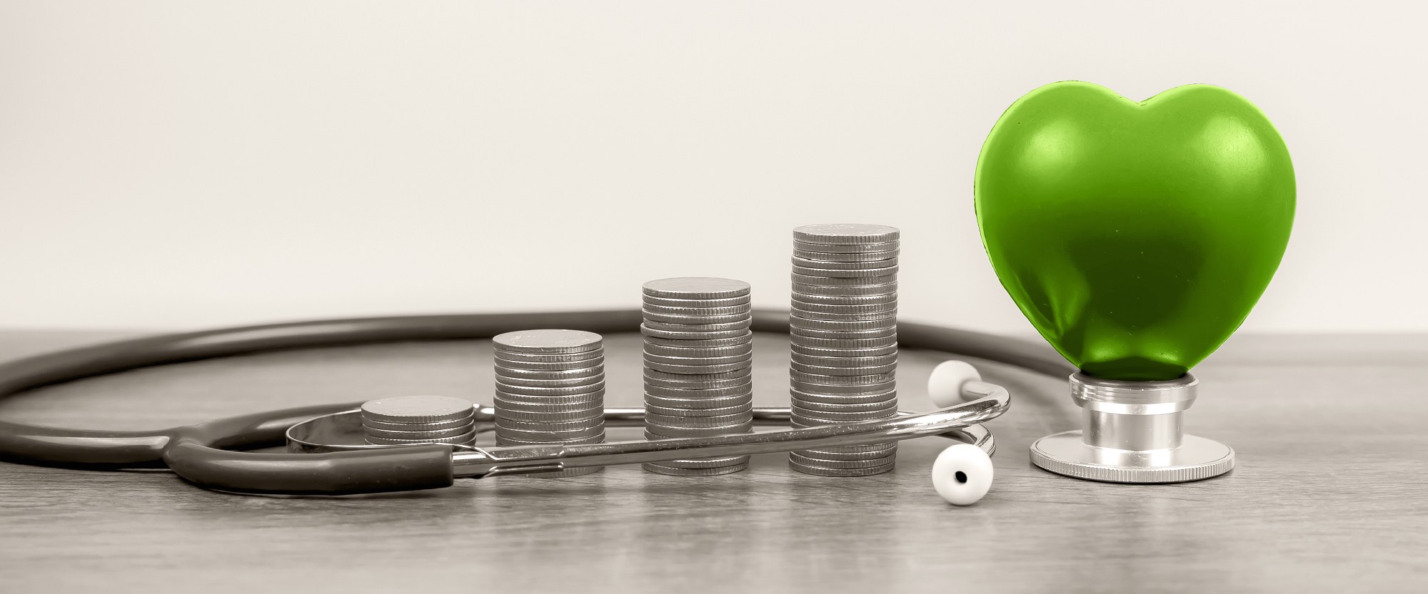 green heart on a stethescope next to stacks of coins