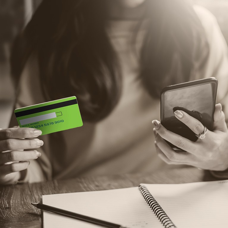 Woman at desk holding credit card and looking at phone