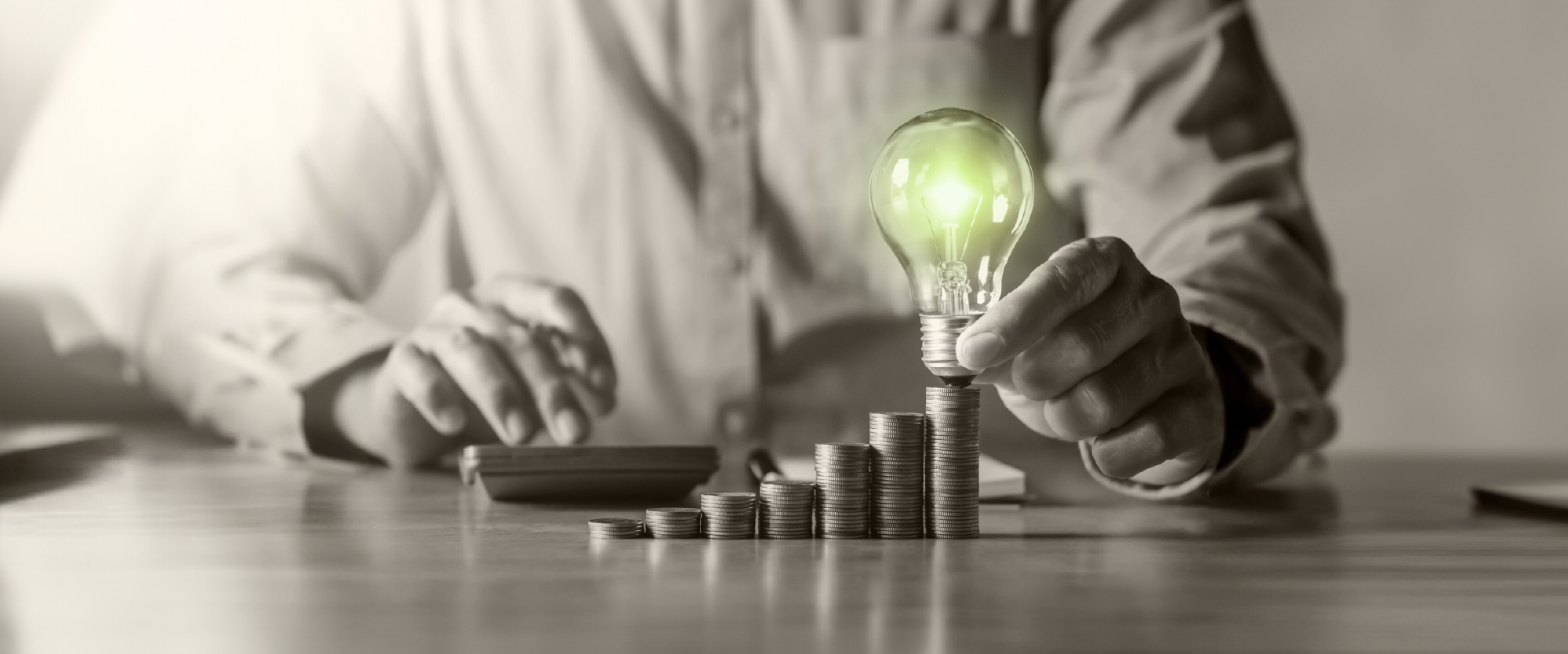 stacks of rising coins with a bright green lightbulb on top of the highest stack