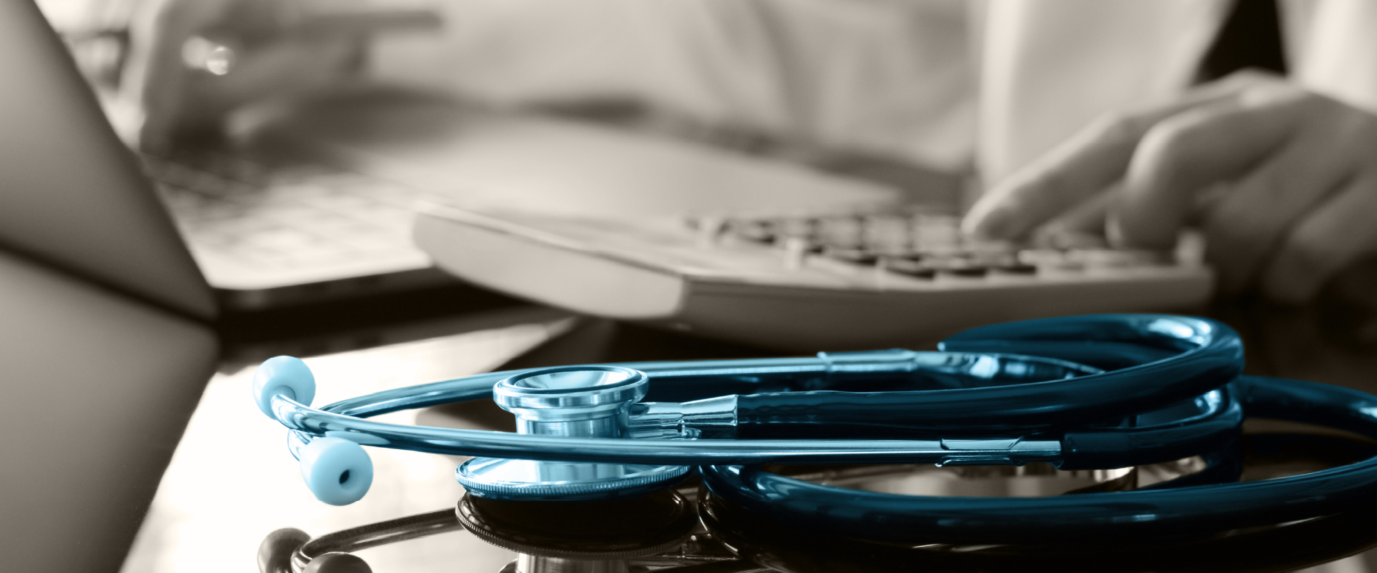 blue stethoscope next to someone working on a laptop with calculator next to it