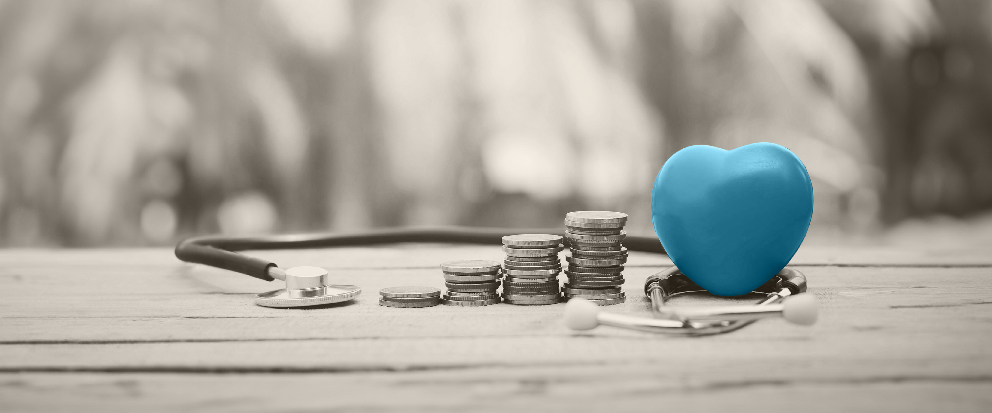 blue heart wrapped by a stethoscope on a desk with money