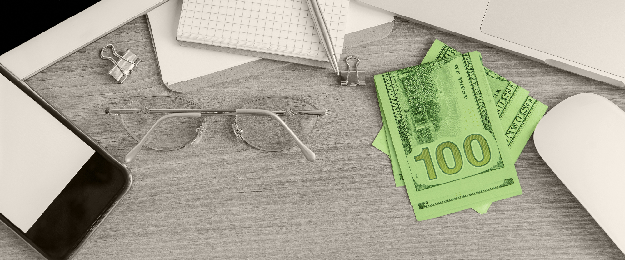 green cash on a table next to a notebook pen and computer